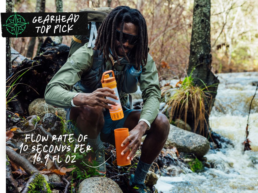 A man beside a creek wearing a pack puts a bottle back together after filling it with water. Text overlay reads: Gearhead top pick, flow rate of 10 seconds per 16.9 fl oz.